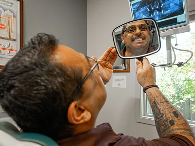 Patient checking his smile in a hand mirror from the dental chair