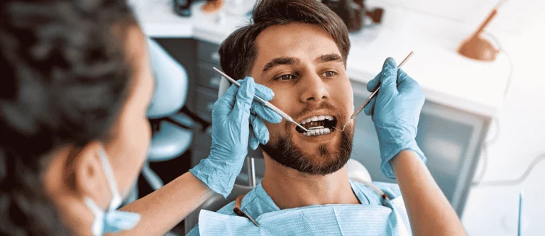 Dentist examining a smiling man’s teeth with a dental mirror