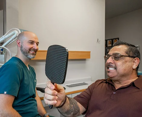 Dentist watching a smiling patient check his teeth in a hand mirror